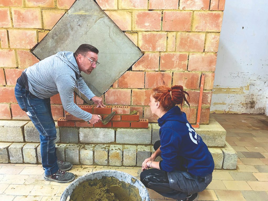 Formateur montrant a une étudiante comment poser des briques et du ciment