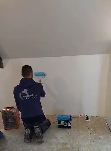 Etudiant qui peint un mur en blanc à l'aide d'un rouleau